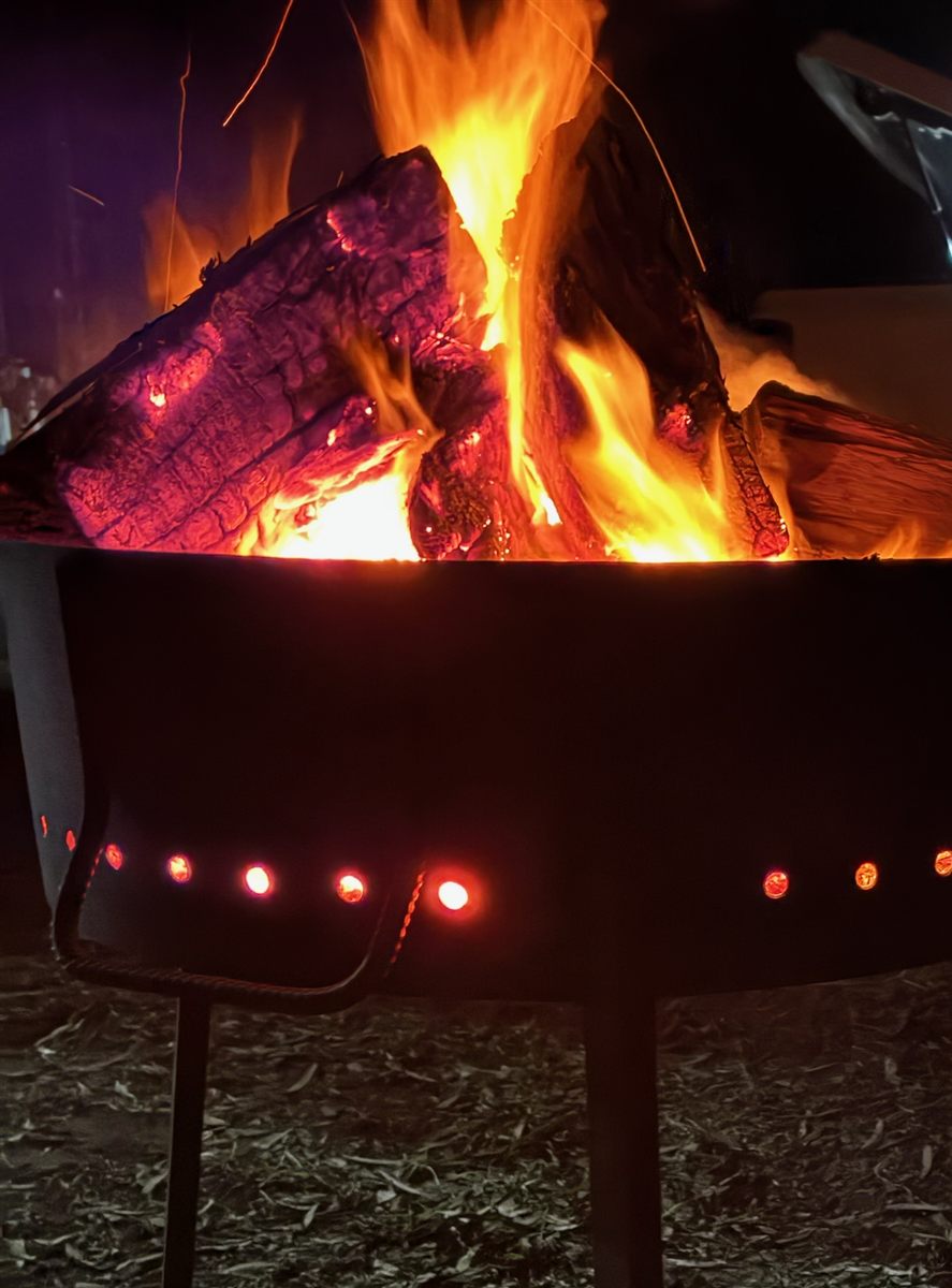 Close-up of the SpareGrills firepit at night, flames above the steel bowl and vent holes glowing